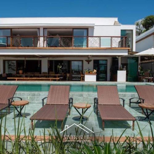 Casa de alto padrão em frente ao mar em Arraial d’Ajuda, com arquitetura moderna, ampla varanda com vista, piscina com borda rasa e espreguiçadeiras, área gourmet integrada e ambiente externo sofisticado.