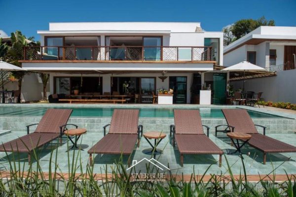 Casa de alto padrão em frente ao mar em Arraial d’Ajuda, com arquitetura moderna, ampla varanda com vista, piscina com borda rasa e espreguiçadeiras, área gourmet integrada e ambiente externo sofisticado.